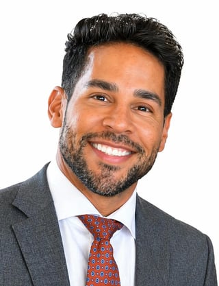 Professional headshot of a smiling man with dark hair and beard wearing a gray suit and red patterned tie against a white background